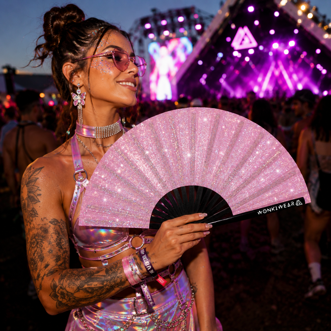 Festival attendee using pink glitter festival fan at outdoor music festival