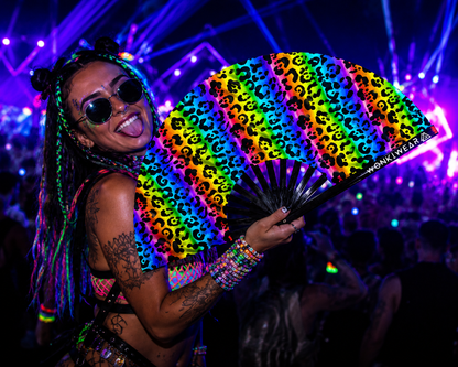 Person holding UV reactive rainbow leopard print rave fan at festival