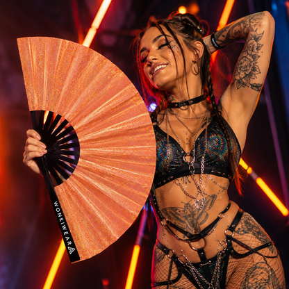 Festival attendee using Venus Galaxy holographic metallic orange festival fan at an outdoor music festival