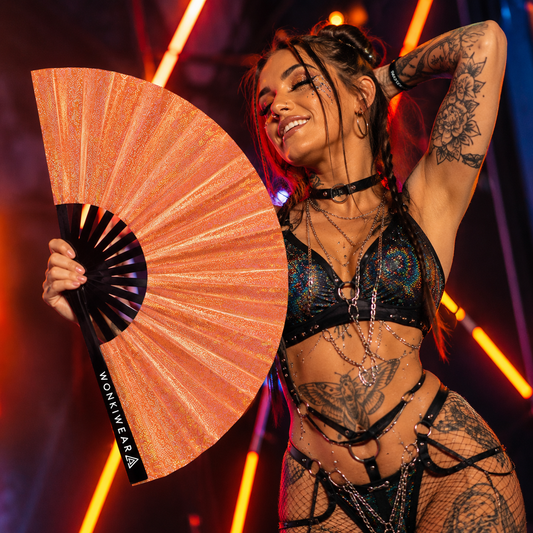 Festival attendee using Venus Galaxy holographic metallic orange festival fan at an outdoor music festival
