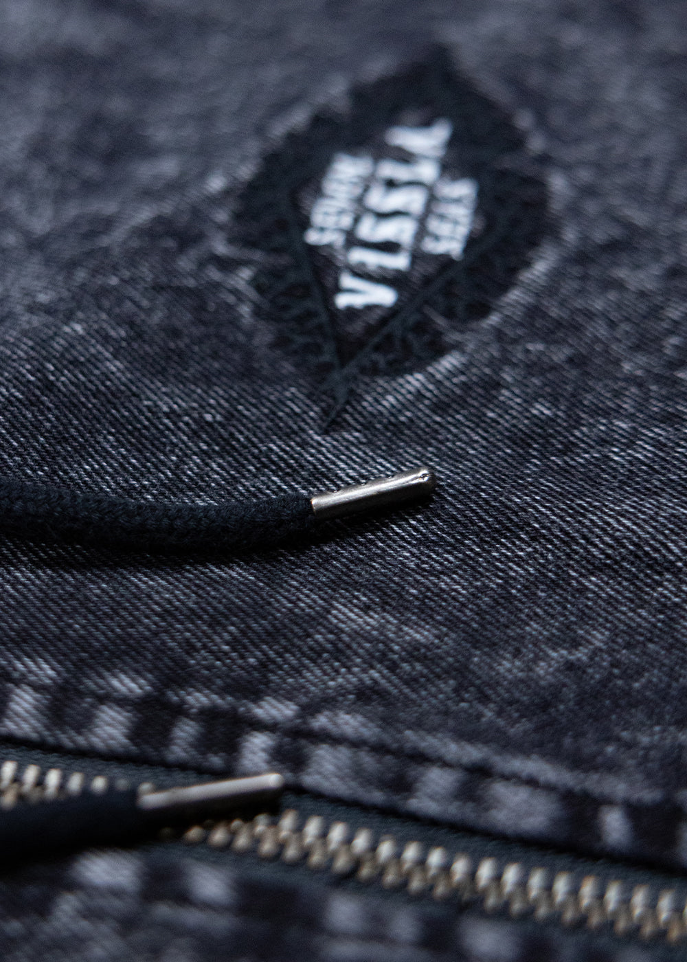 Close-up of the Vissla chest logo and metal zip on the black acid-wash Wasson jacket