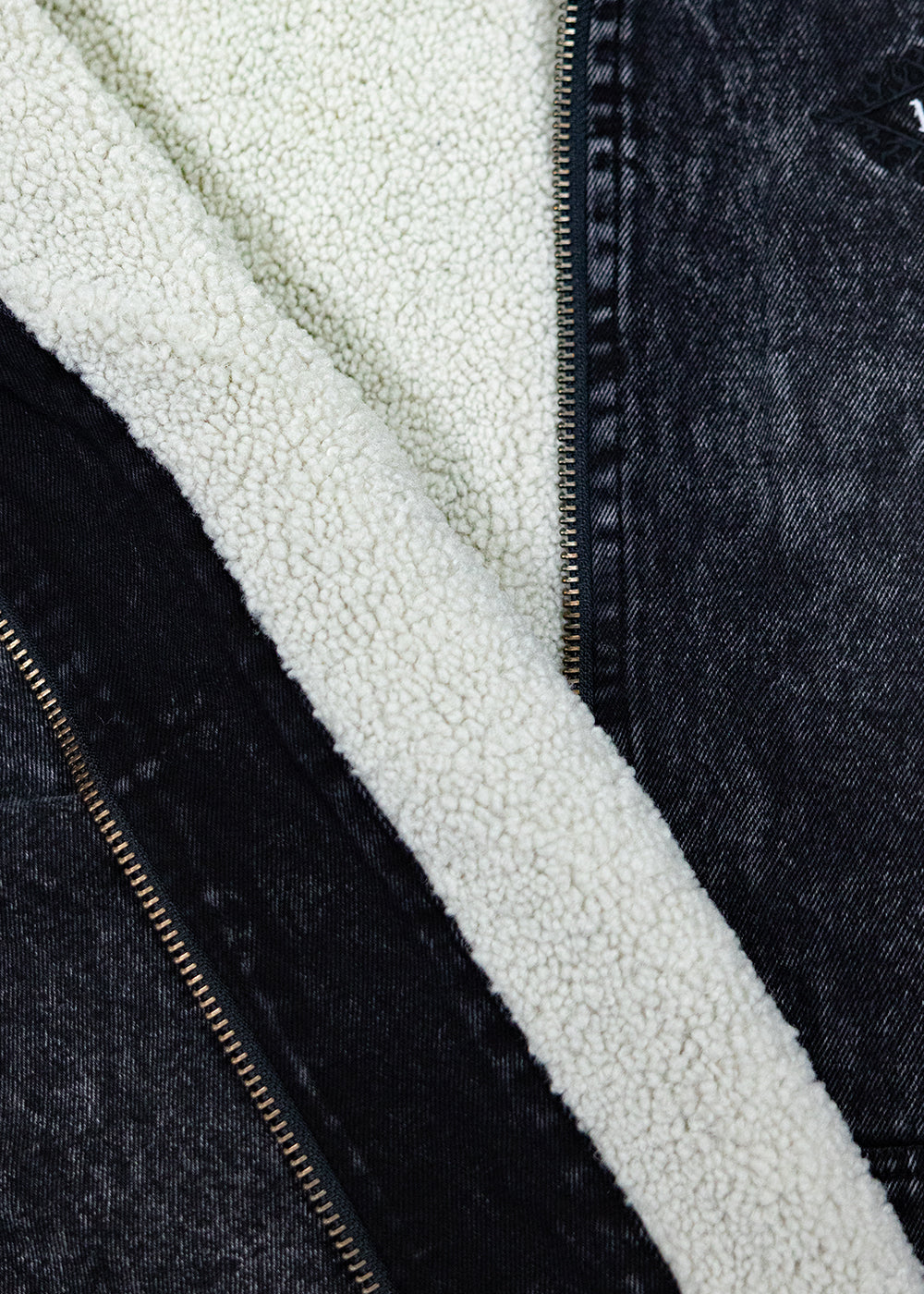 Close-up showing the cream sherpa lining beside the black acid-wash denim outer