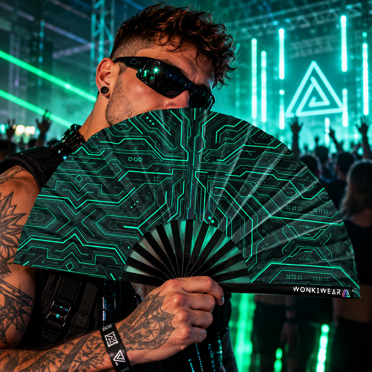 Man dancing at an underground techno rave holding a black folding fan with teal Cyber Circuit graphics and WonkiWear branding.