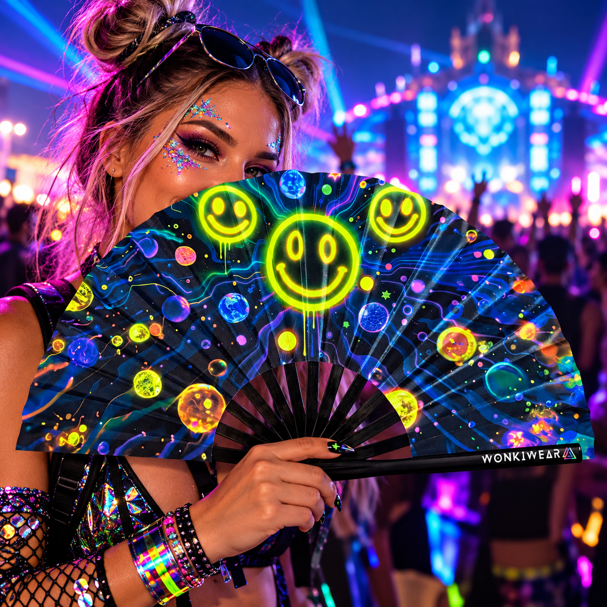 WonkiWear galaxy smiley face folding fan held by a festivalgoer at a neon-lit rave.