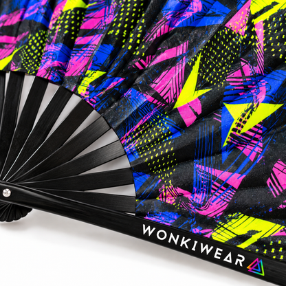 Close-up macro of a WonkiWear black folding rave fan featuring vibrant hot pink, electric blue and neon yellow-green geometric print, with glossy black ribs and the WonkiWear logo on the outer rib.