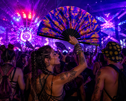 Festival crowd using UV reactive trippy orange and blue rave fan under event lighting