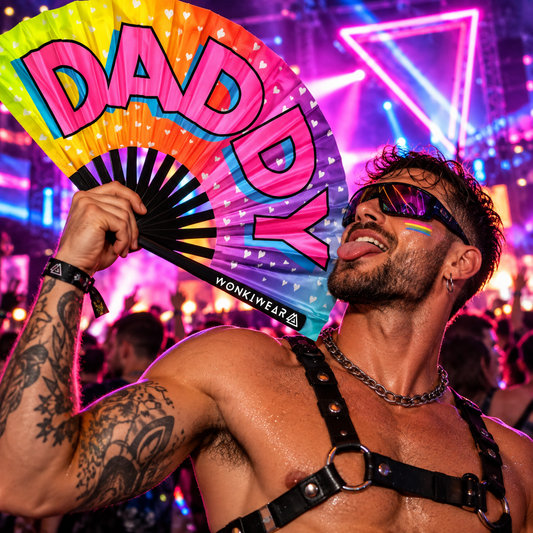 Male techno raver holding a colourful XL rainbow folding fan with bold pink “DADDY” lettering at a neon rave.