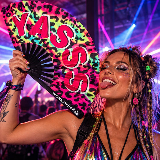 Raver holding a large XL rainbow leopard-print folding fan with “YASSS” lettering at a colourful neon festival.