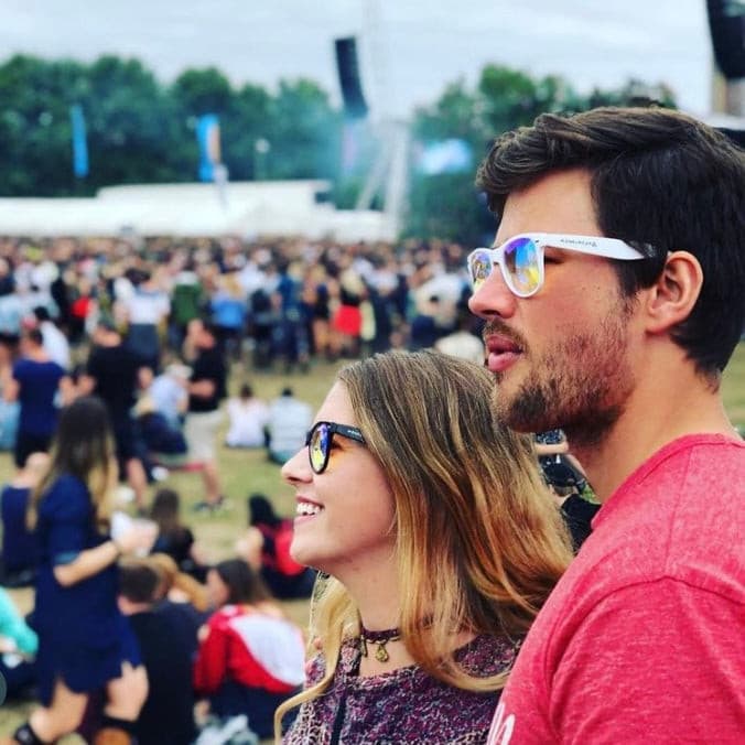 Couple wearing wayfarer kaleidoscope glasses at a festival with prism light effects in a crowd setting